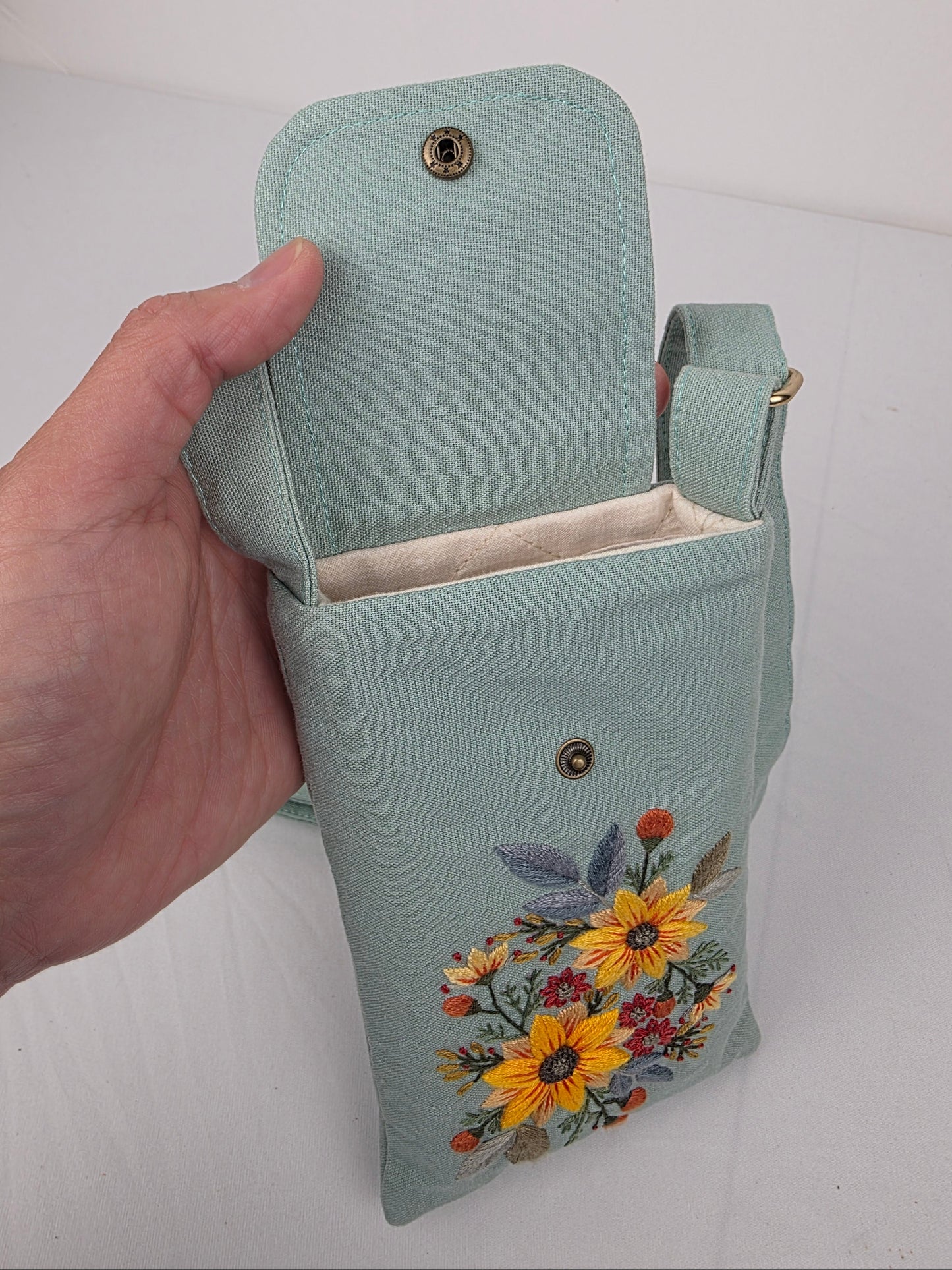 Light blue clutch with floral embroidery held by a hand on a white background