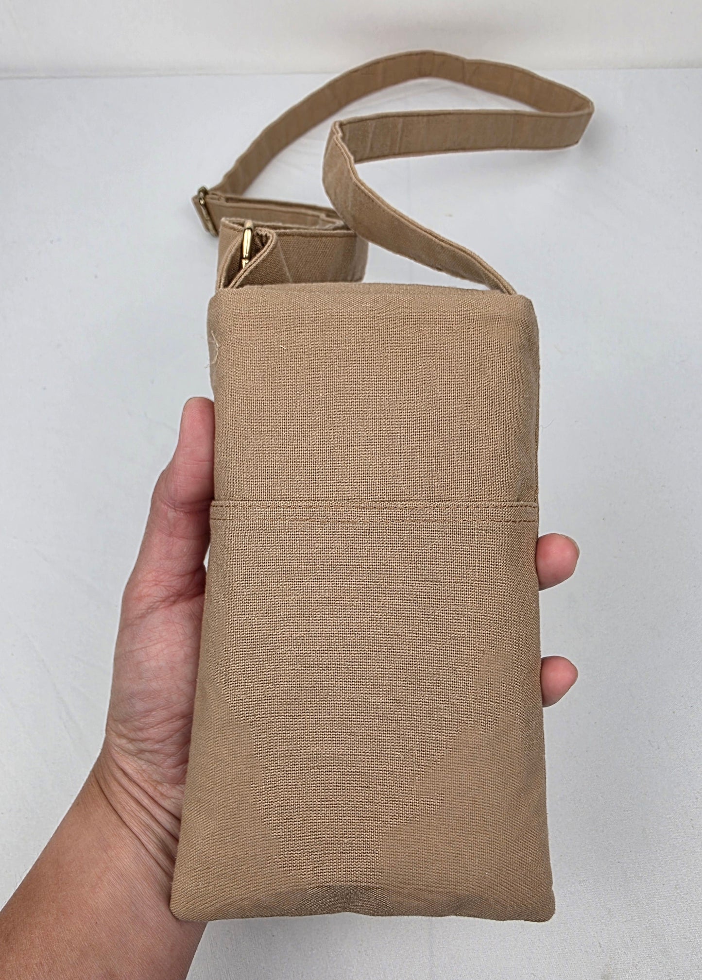Beige crossbody bag held by a hand against a white background