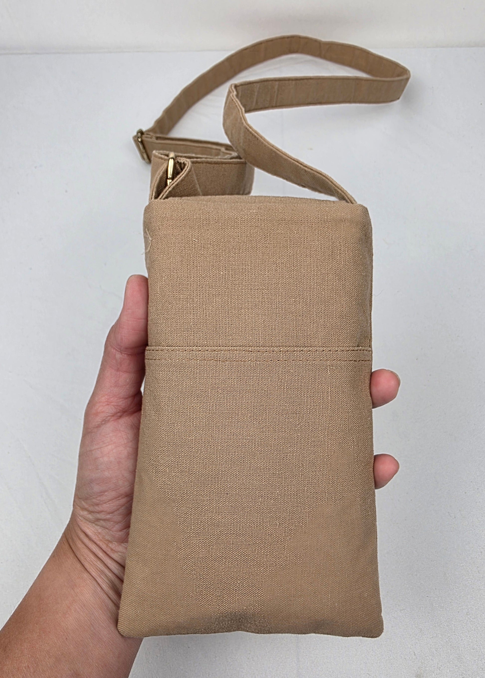 Beige crossbody bag held by a hand against a white background